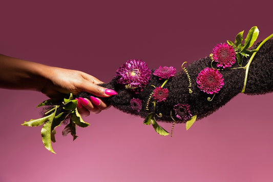 Black woman holding textured hair extensions with pink flowers and green leaves intertwined